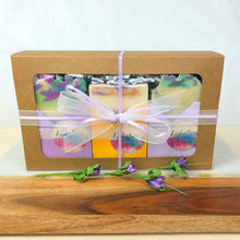 Load image into Gallery viewer, Kraft paper gift box holding three handmade luxury soap bars. Colors of purple and yellow. Tied with a purple and white ribbon.
